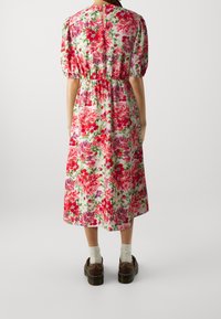 Kukallinen midi-mekko, jossa on lyhyet puffihihat. Mekossa on punaisia, pinkkejä ja vihreitä kukkia valkoisella taustalla. Mekossa on elastinen vyötärö ja takana nappikiinnitys.