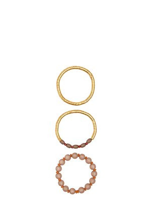 Trzy bransoletki z koralików ułożone pionowo: złote koraliki na górze, złote z brązowymi i czerwonymi koralikami na środku, okrągłe beżowe koraliki z pomarańczowymi przekładkami na dole.