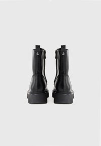Stivali alla caviglia in pelle nera con una texture liscia, cerniere laterali e suole in gomma nera spessa. Presentano hardware minimale e un design elegante.