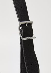 Bracelet en cuir noir avec une finition texturée. Présente une boucle en métal argenté et des trous ajustables pour personnaliser la taille.