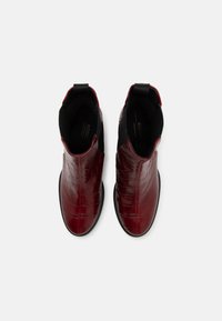 Bocanci ankle roșii, din piele lucioasă, cu un model de crocodil, părți elastice și talpă plată neagră. Textură netedă cu o formă aerodinamică.
