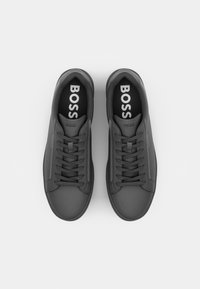 Baskets grises en matériau lisse, bout arrondi et lacets plats. Logo "BOSS" en blanc sur les semelles intérieures. Design minimaliste, sans motifs ni accents.