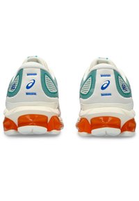 White and teal running shoes with orange soles, featuring textured mesh panels, bold branding, and a cushioned heel design.