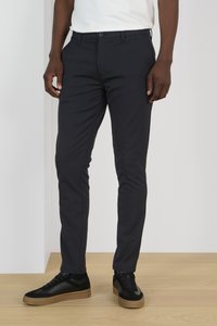 Pantalones de corte slim de color navy, confeccionados en tejido ligero, con bolsillos delanteros, trabillas para cinturón y cierre de botón, combinados con zapatillas negras.