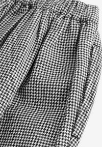 Mustvalge houndstooth mustriga kangas, millel on kogutud vöökoht, pehme tekstuur ja voolavad voldid.