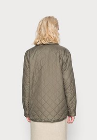 Oliven grøn quiltet jakke med krave, lange ærmer og lige kant. Stoffet har en glat tekstur med diamantstik.