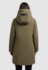 Oliwkowy długi płaszcz z kapturem, z pikowanym wzorem, bocznymi kieszeniami i czarną naszywką z logo u dołu. Gładka, matowa faktura.