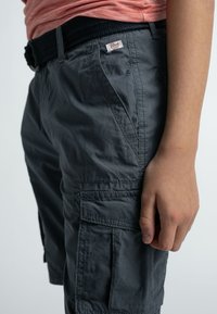 Harmaat cargo-shorts, jotka on valmistettu kevyestä kankaasta ja joissa on useita taskuja sekä teksturoitu vyötärö. Suunnittelu on käytännöllinen ja rento.