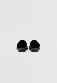 Black leather backless mules with a flat sole and rounded opening. The texture is smooth with subtle stitching details along the edges.