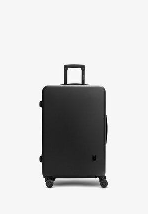 Black hard-shell suitcase with telescopic handle extended and four spinner wheels on white background.