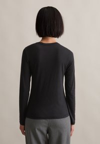 Czarna koszula z długim rękawem o okrągłym dekolcie, wykonana z miękkiego materiału, w zestawie z szarymi spodniami w prążki, widok z tyłu.