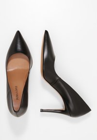 Černé kožené lodičky na vysokém podpatku s špičatou špičkou, hladkou strukturou a štíhlým siluetou s nízkým dekoltem vpředu.