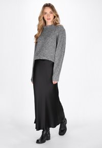 Grijze cropped sweater met een zachte textuur, gecombineerd met een zwarte satijnen maxi-rok en chunky zwarte haklaarzen met hardwareaccenten.