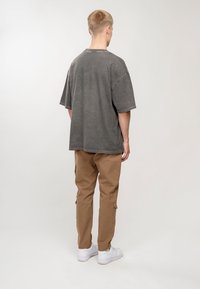 Übergroßes graues T-Shirt mit kurzen Ärmeln, kombiniert mit beigefarbenen Cargo-Hosen mit seitlichen Taschen und weißen Turnschuhen. Minimale Textur.