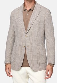 Ljusbrun rutig kavaj i strukturerad tyg, med två knappar, utsvängda slag och två framfickor, tillsammans med en brun polo-tröja.