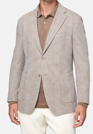 Blazer a quadri marrone chiaro realizzato in tessuto testurizzato, caratterizzato da due bottoni, rever a taglio e due tasche anteriori, abbinato a una polo marrone.
