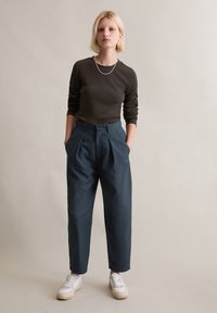 Haut marron à manches longues, pantalon taille haute bleu foncé avec plis, baskets blanches. Design simple, texture lisse, coupe décontractée.