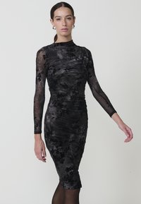 Rochie din catifea neagră cu imprimeu floral, cu mâneci lungi din material transparent, siluetă ajustată și textură fronsată. Guler înalt și tiv până la genunchi.