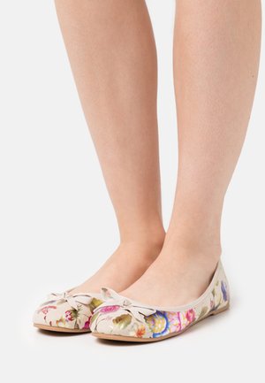 Paire de ballerines beiges à motif floral avec petits nœuds, portées pieds nus sur un fond blanc uni.