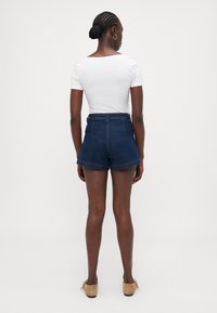 Høyt liv mørk denim shorts med rullekanter, parret med en tettsittende hvit kortermet topp. Enfargede, minimal detaljer.