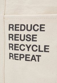Cotton tote bag with a natural off-white color featuring bold black text: “REDUCE, REUSE, RECYCLE, REPEAT” arranged vertically.