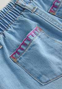 Denim bleu clair avec une ceinture élastique et une poche arrière ornée d'une couture en zigzag rose sur le bord supérieur.