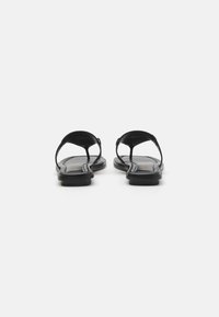 Sandali in pelle nera con suola piatta, design open toe e cinturini regolabili. Presentano una texture liscia e uno stile minimalista.