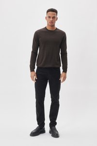 Donkerbruin lange mouwen sweater, slim fit, ronde halslijn, gecombineerd met zwarte slim-fit broek en zwarte instappers, staande op een witte achtergrond.
