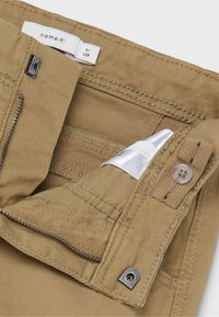 Pantaloni khaki con zip, chiusura a bottone e molteplici tasche interne con cuciture a contrasto e una morbida texture del tessuto.