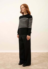 Czarny sweter z poziomymi białymi paskami, prążkowana struktura, okrągły dekolt; zestawiony z szerokimi czarnymi spodniami i czarnymi butami.