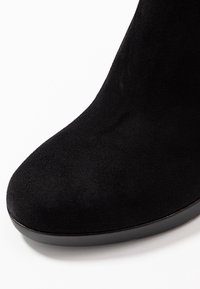 Stivale alla caviglia in suede nero con punta arrotondata e superficie liscia e testurizzata. La suola è nera con una leggera curvatura nella parte anteriore.