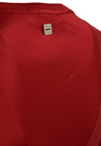 Top in tessuto rosso con una texture liscia e opaca, dotato di un piccolo tag metallico del marchio vicino al colletto. Design semplice, senza motivi o decorazioni.