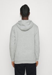 Sudadera con capucha gris con un acabado texturizado, que presenta una capucha con cordón y puños acanalados, mostrada desde atrás.