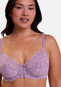 Reggiseno in pizzo lavanda con motivo floreale, bordi scallop e dettaglio incrociato sul davanti. Spalline sottili e regolabili per un aspetto delicato.