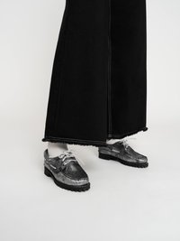 Schwarze Denim-Hose mit weitem Bein und ausgefransten Säumen, kombiniert mit grauen Lederschuhen mit strukturiertem Finish, runder Zehenform und weißen Schnürsenkeln.