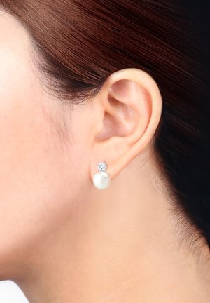 Boucles d'oreilles en perles présentant une perle blanche ronde avec un petit accent en pierre précieuse claire au-dessus, montées sur un métal argenté.