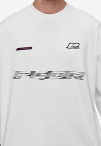 White long-sleeve shirt featuring black and pink graphic prints. Material appears soft, with a relaxed fit and ribbed collar.