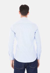 Camicia a maniche lunghe a righe in cotone azzurro chiaro e bianco. Presenta un colletto sagomato, polsini con bottoni e un orlo dritto.