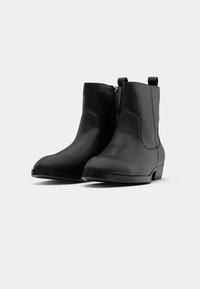 Pár čiernych kožených členkových topánok so bočnými zipsami a úchytmi, zobrazených na jednofarebnom bielom pozadí.