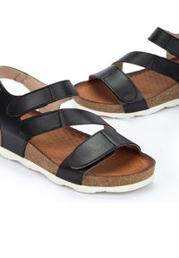 Sandalias negras con tres correas ajustables, plantilla de corcho, suela interior texturizada marrón y suela exterior de caucho blanca. Adecuadas para uso casual.