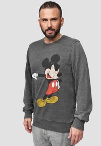 Grijze sweatshirt met een voorzijde grafiek van Mickey Mouse in rode shorts en gele schoenen. Ribbelkanten mouwen en zoom voegen textuur toe aan het ontwerp.