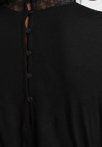 Czarny strój z wysokim, koronkowym kołnierzem i zapięciem na guziki z tyłu. Posiada sześć małych guzików materiałowych wzdłuż pionowej listwy. Gładka tekstura.