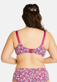Soutien-gorge à motif floral dans des tons de rose, avec des bretelles ajustables et une attache à crochet. Le tissu a une texture lisse et des accents colorés.