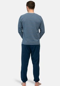 Lange mouw navy en witte gestreepte top in combinatie met donkerblauwe trainingsbroek. Zacht stof, relaxte pasvorm en elastische boorden op de broek.