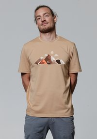 Beige t-shirt met een bergafbeelding in tinten bruin, oranje en wit, met korte mouwen en een ronde hals.