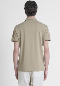 Beige poloshirt van gladde stof, met een klassieke kraag en korte mouwen met donkere accenten aan de randen.