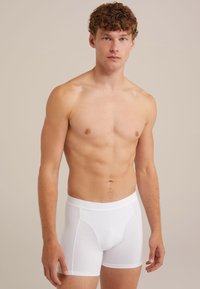 Boxers blancs présentés sur un modèle masculin, en coton doux avec une ceinture élastique comprenant un détail de logo.