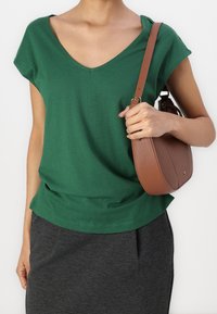 T-shirt verde in cotone con scollatura a V profonda e maniche a cappuccio, abbinato a una gonna grigia. Una borsa a tracolla marrone pende su una spalla.