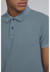Kortærmet polo-shirt i blødt, afdæmpet blåt stof. Har en klassisk krave, to-knap lukning og struktureret vævning.