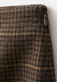 Rjava karirana tkanina z teksturiranim tkanjem. Ima temno in svetlo rjave vzorce, zipper na strani ter mehak, puhast površin.